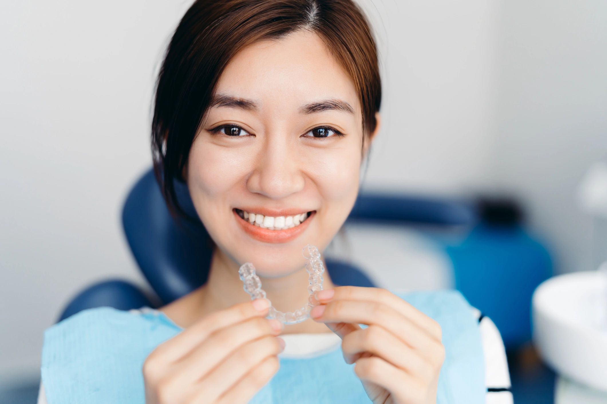 Asian woman holding clear aligners in a dental clinic